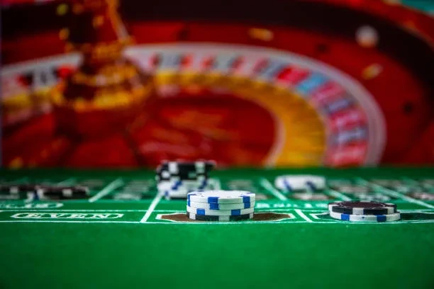 View of a roulette wheel and several chips of different colors on a green casino table.